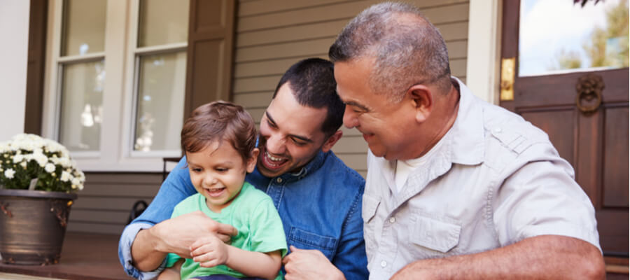 An older man sitting beside his son looking at his grandson together