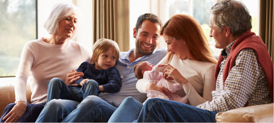 Grandparents sitting with a couple holding a newborn baby with their toddler son