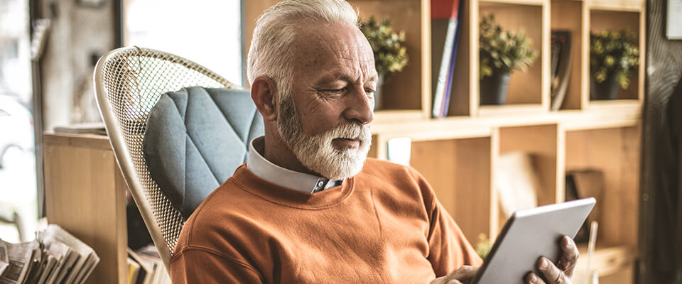 An older man sitting and looking at his tablet