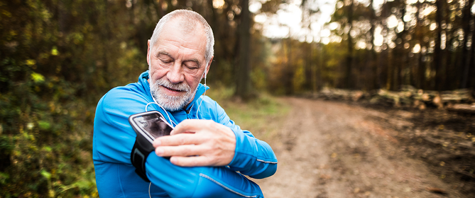 An older man jogging on a path changing the setting to his mobile device